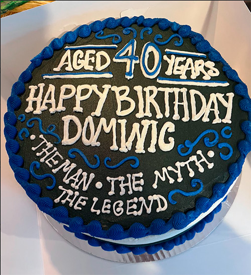 A round black and blue cake that says Aged 40 Years, Happy Birthday Dominic, the man, the myth, the legend