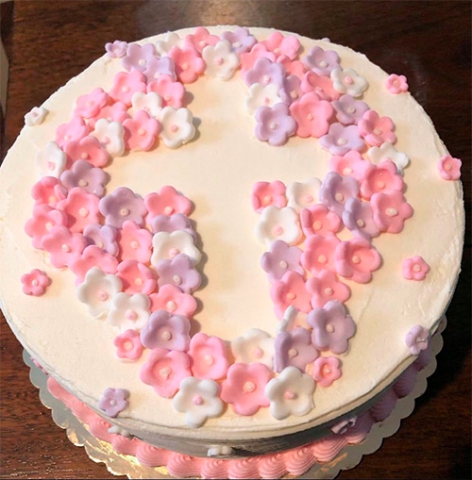 A round cake displaying an inverted cross with pastel pink and lavender colored flowers