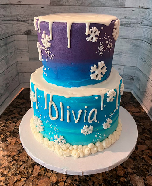 a Frozen themed two tiered cake with the name Olivia on the side of the bottom tier