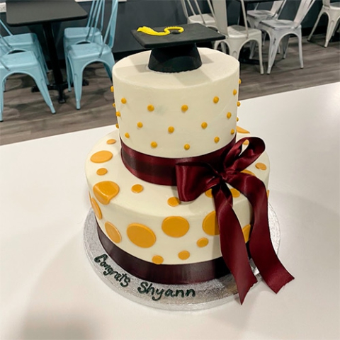 a two tiered cake with a graduation cap on top and yellow polka dots on the side of the botton tier