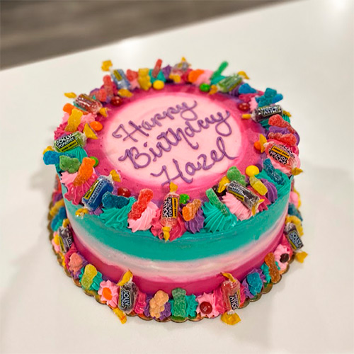 A colorful jolly rancher and sour patch kid flavored cake with the words Happy Birthday Hazel on top