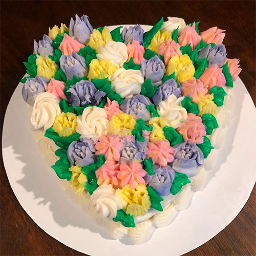 a heart shaped cake with pink, yellow, purple and white tullip shaped flowers on top