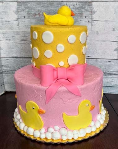 a two tiered pink and yellow cake with rubber duckies on the side and top