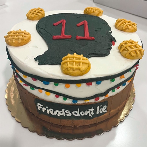 A Stranger Things inspired round cake with the number 11 and waffles on top. the words Friend don't lie are displayed on the side
