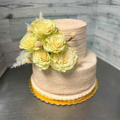 a two tiered taupe brown cake with artificial yellow roses sticking out on the side